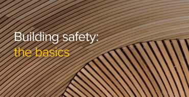 Text on a background of curved wooden slats reading Building safety: the basics in stylised font, suggesting a focus on foundational elements of construction safety and design.