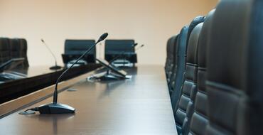 Empty boardroom with black leather chairs and microphones on a polished wooden conference table, suggesting a professional corporate meeting environment.